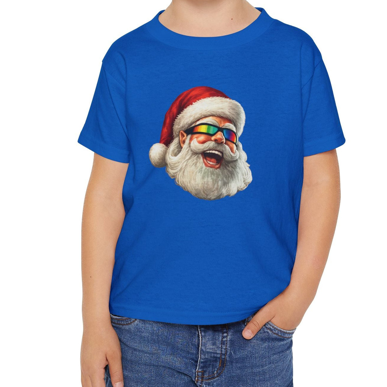 A young child wearing a bright blue short-sleeve t-shirt with a graphic print of the A Totally Awesome Radical Christmas Santa face, paired with blue jeans, set against a plain white background.
